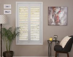 a living room filled with furniture and windows covered in white plantation shutters next to a lamp