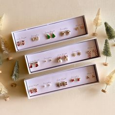 three pairs of earrings sitting in a box next to christmas trees and pine cones on a table