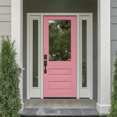 a pink front door on a gray house with white trim and two bushes next to it