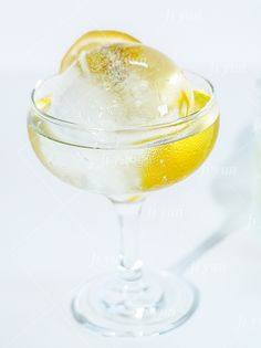 a glass filled with ice and lemon on top of a white table next to a bottle