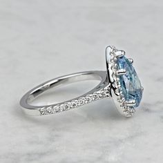 an oval cut blue topaz ring on a marble surface with diamonds around the band