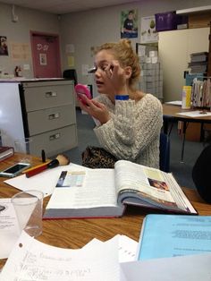 a woman sitting at a desk with an open book and cell phone in her hand