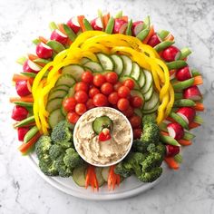 a platter filled with vegetables, dip and veggies on top of a marble table