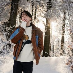 a man standing in the snow with his hand on his mouth and wearing a brown jacket