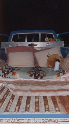 an old bed in the back of a pick up truck with pillows and blankets on it