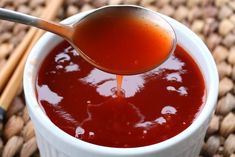 a spoon full of sauce being poured into a white cup with cinnamon sticks in the background