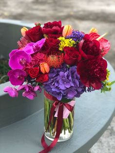 a vase filled with lots of colorful flowers on top of a blue table next to a park bench