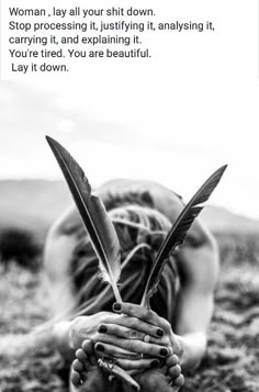 a woman laying on the ground with her hands over her face while holding a feather