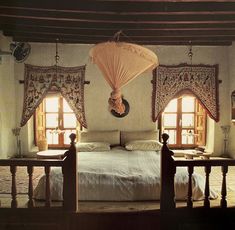 a bed room with a neatly made bed next to two windows and a ceiling fan