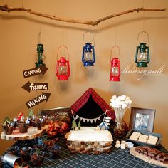 a table topped with cakes and desserts next to hanging signs that spell out camping