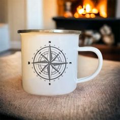 a white coffee cup with a compass design on it sitting in front of a fire place