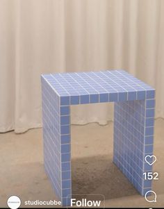 a small blue tiled table sitting in front of a white curtain with the words studiocube follow below it