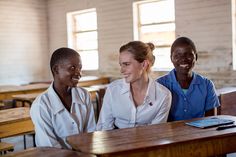 three women sitting at a table smiling for the camera in a school room with wooden desks