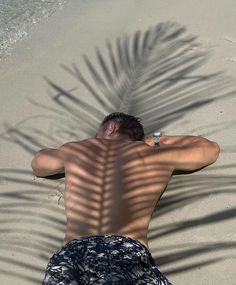 a man laying on top of a sandy beach next to the ocean under a palm tree