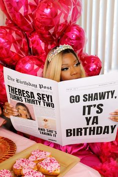 a woman reading a magazine about her birthday with pink balloons and donuts in the background