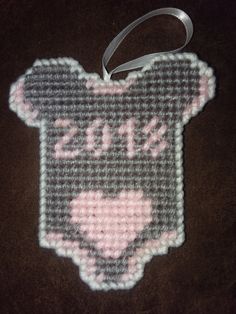 a cross stitch ornament hanging from a ribbon on a table with a black background