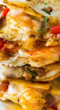 a stack of quesadillas on a white plate with tomatoes and green peppers