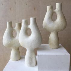 three white vases sitting on top of a white pedestal in front of a wall