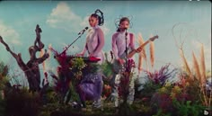 two women standing on top of a lush green field next to each other holding guitars