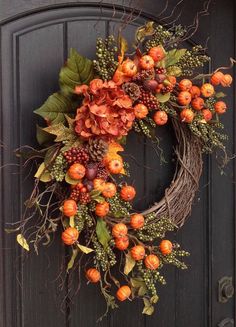 a wreath with orange flowers and green leaves hangs on a door handle, in front of a black wooden door