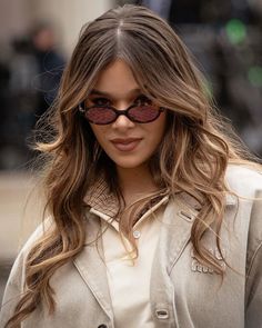 a woman with long hair wearing sunglasses and a trench coat is looking at the camera