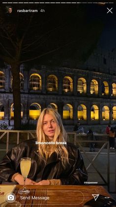 a woman sitting at a table with a glass of wine in front of an old building