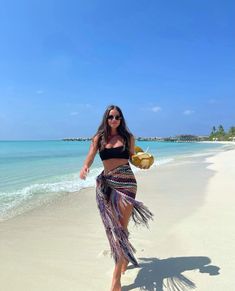 a woman is walking on the beach wearing a skirt