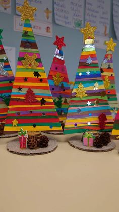 three brightly colored christmas trees with presents in front of them on a table next to other decorations