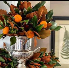 a silver vase filled with oranges and greenery