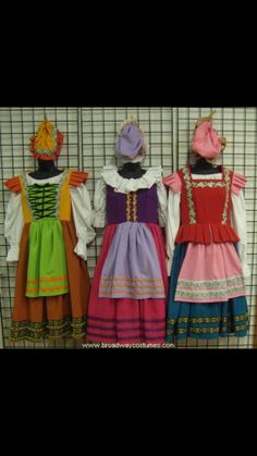 three children's dresses are lined up against a wire fence, one is colorful and the other is multicolored