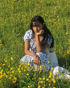 a woman sitting in the grass with her hand on her chin