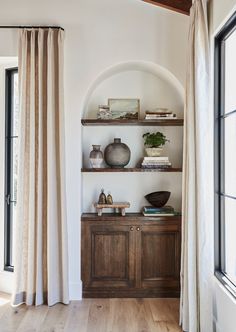 a wooden cabinet sitting in front of a window filled with books and vases on top of it