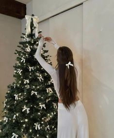 a woman is decorating a christmas tree with white bows on her head and hands