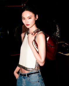 a young woman is standing in the dark with a handbag on her shoulder and looking at the camera