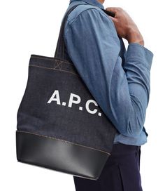 A.P.C. tote bag. - Tote bag in Japanese denim.- Two large handles. May be carried on shoulder or by hand.- Wide band in smooth leather on bottom of bag.- Reinforced base.- Interior zip pocket.- Large A.P.C. logo in front.- Caramel topstitching on the denim.- Small version of the Axelle tote bag. Medium Shoulder Bag With Leather Handles For Shopping, Medium Shoulder Bag With Large Capacity For Shopping, Chic Medium Shoulder Bag With Large Capacity, Chic Large Capacity Shoulder Bag, Tan Medium Shoulder Bag For Everyday Use, Everyday Medium Tan Bag, Medium Tan Everyday Bag, White Shirt Men, White Shirts Women