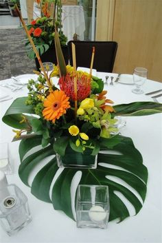 an arrangement of flowers and greenery on a white table cloth with candles in the center