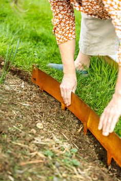 a woman bending over to pick up some grass from the ground with her hand on top of a piece of wood