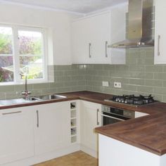 a kitchen with white cabinets and wooden counter tops next to a stove top oven under a window