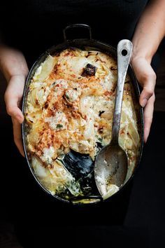 a person holding a pan with some food in it and a spoon next to it