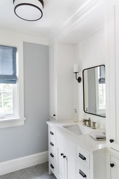 a white bathroom with gray walls and black hardware on the vanity, along with a large mirror