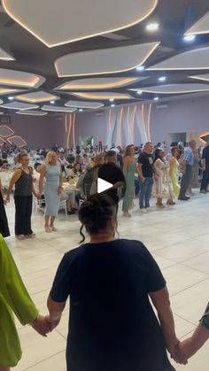 two women hold hands as they walk through a large room filled with people in dresses