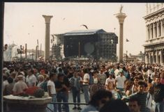 a large group of people standing around in front of a stage with birds flying overhead