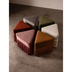 four different colored stools with fringed ends on the floor in an empty room