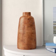 a brown vase sitting on top of a white shelf next to a blue and white book