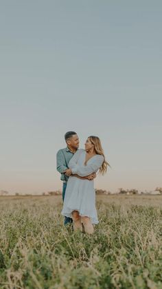 a man and woman standing in the middle of a field with their arms around each other