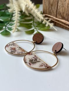 two circular earrings with floral designs on them sitting next to a plant and some leaves