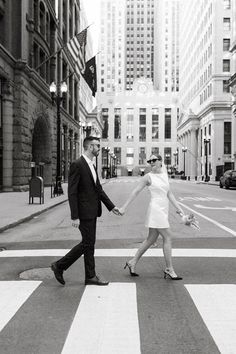 a man and woman walking across a crosswalk in the middle of a city holding hands