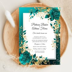 a green and gold wedding card on top of a wooden plate next to a feather