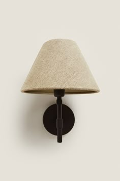 a wall light with a beige shade on it's side and a black base