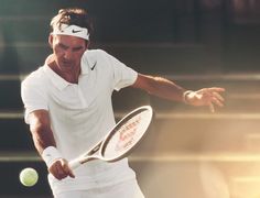 a male tennis player is swinging his racket to hit the ball with both hands